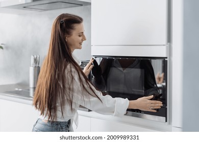 Smiling Young Woman Closing Electric Microwave Door After Putting Food Inside, Female Using New Modern Kitchen Appliances While Preparing Dinner For Family At Home