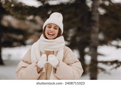 Smiling young woman with coffee hot drink cup enjoys winter weather at snowy winter park - Powered by Shutterstock