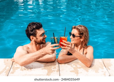 Smiling young woman and a cute dark-haired guy clinking glasses of cocktails in an outdoor swimming pool. Leisure and summer vacation concept - Powered by Shutterstock