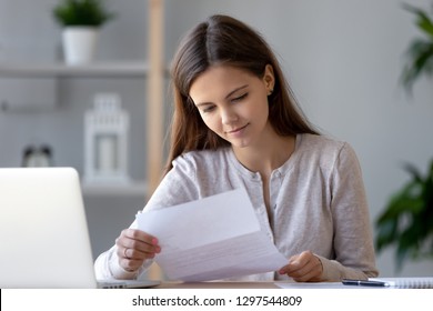 Smiling Young Woman Doing Paperwork Holding Letter Of Advice Bill Reading Paper Checking Post Mail At Home, Female Customer Receiving Notification Statement Receipt From Bank Satisfied With Good News