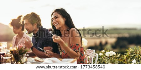 Smiling young woman eating food and talking with friends during a dinner party outdoors. Woman enjoying having food with friends at a party.