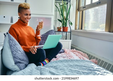 Smiling Young Woman Enjoying Drinking From Champagne Flute While Video Calling Through Laptop At Home