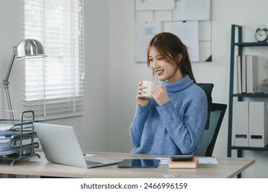 Smiling young woman enjoying a warm beverage during a break in a modern home office - Powered by Shutterstock