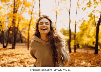 Smiling young woman enjoys the autumn weather in the forest with the yellow leaves at sunset - Powered by Shutterstock