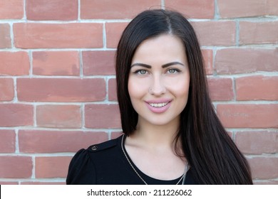 Smiling young woman in front of modern brick wall, a lot of space for text. Young 20s brunette head and shoulders front view against red brick wall, a lot of copyspace.