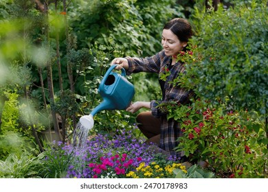 smiling young woman gardener water the flowers from watering can in garden. Hobby concept of growing and taking care of plants at backyard