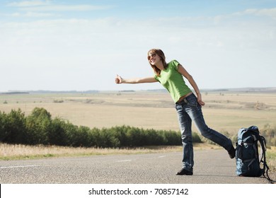 Smiling Young Woman In Glasses Hitch Hicking On A Road