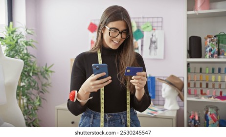 Smiling young woman with glasses and measuring tape using smartphone and credit card in a tailor shop. - Powered by Shutterstock