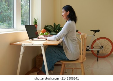 Smiling Young Woman With Good Posture Wearing Domestic Clothes When Working On Laptop At Home