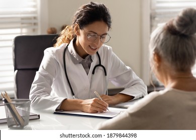 Smiling Young Woman GP Write Prescription To Mature Patient At Consultation In Hospital. Female Doctor Consult Talk With Elderly Client In Private Clinic. Healthcare Insurance, Geriatrics Concept.