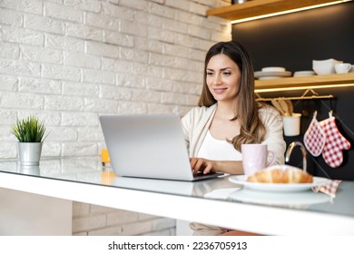 Smiling young woman having breakfast  while working on laptop at home. Work from home concept.