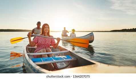 Smiling young woman and her boyfriend enjoying a day canoeing with friends on a lake on a late summer afternoon - Powered by Shutterstock