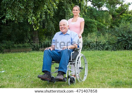 Smiling Young Woman With Her Disabled Father On Wheelchair In Park