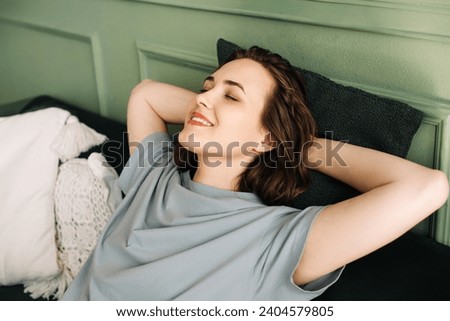 A smiling young woman with her eyes closed is lying on a couch, enjoying some rest and sleep. Serenity Unveiled. Relaxed Young Woman Rests Peacefully on Sofa. Blissful Slumber.