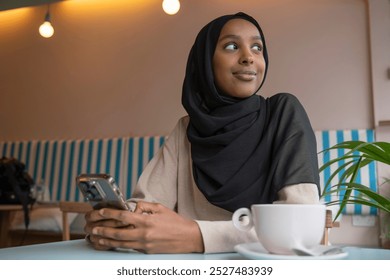 Smiling young woman in hijab using phone in cafe - Powered by Shutterstock