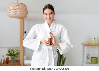 Smiling Young Woman Holding Bottle Of Natural Essential Oil In Bathroom