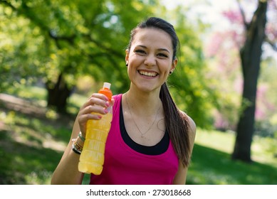 Smiling Young Woman Holding Energy Drink Outdoors In A Park.