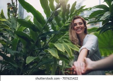 Smiling Young Woman Holding Hand Of Her Boyfriend. POV Shot Of Couple In Tropical Botanical Garden.