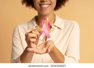 Smiling young woman is holding a pink ribbon, symbolizing hope and support for breast cancer awareness - Powered by Shutterstock