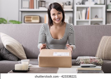 Smiling young woman at home on the couch, she has received a postal parcel, online shopping and delivery concept