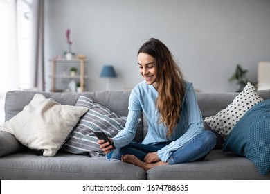 Smiling young woman at home using modern smartphone. Online chat.