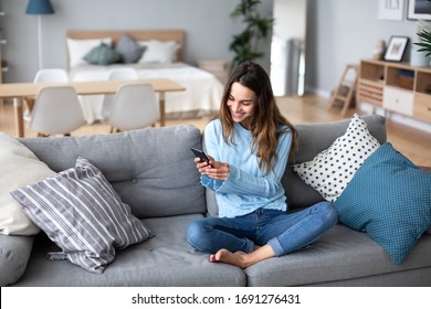Junge Frau zu Hause mit modernem Smartphone lächeln. Online-Chat. Leben im Inland.