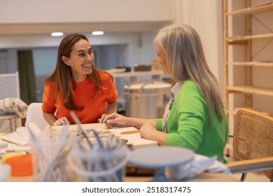 Smiling young woman interacts with an elderly woman while working on pottery in a creative studio. - Powered by Shutterstock