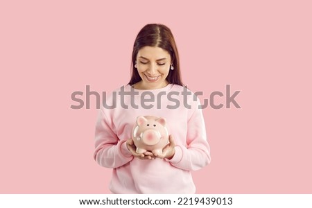 Smiling young woman isolated on pink studio background hold piggy bank care about money saving for future needs. Happy female with piggybank recommend finance collecting. Financial stability, banking.