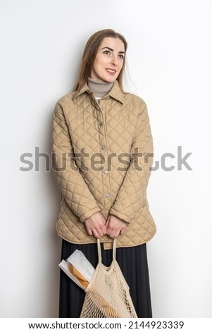 Smiling young woman in a jacket midi skirt with a shopping bag against a white wall