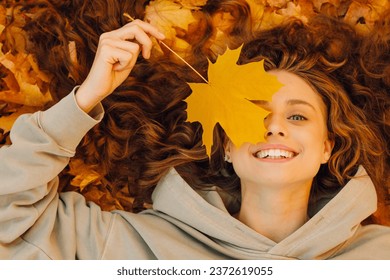 Smiling young woman lies on the autumn foliage in the park with the yellow leaves - Powered by Shutterstock