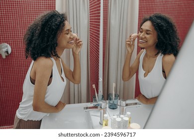 Smiling young woman look in mirror in bathroom while using beauty sponge for making make-up - Powered by Shutterstock