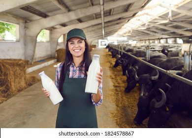 Smiling young woman looking at camera and holding bottles of fresh natural cow buffalo milk standing in barn on dairy farm. Happy farm worker or farming business owner demonstrating organic dairy - Powered by Shutterstock