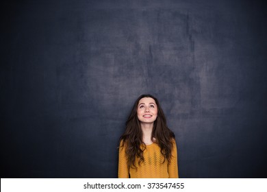 Smiling Young Woman Looking Up At Copyspace Over Black Background