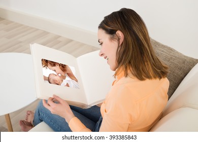 Smiling Young Woman Looking At Photo Album In Her Living Room