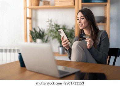 Smiling young woman looking at smart phone screen holding credit card, using mobile phone secured online e-banking app, satisfied with online cashback purchase or good electronic banking services.
