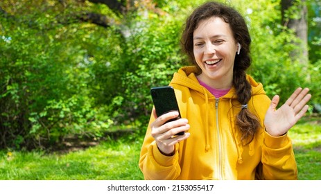 Smiling young woman making video call with mobile phone in green garden outdoors. Best friends having virtual conference, party online meeting use digital application for communication.Gesturing hi. - Powered by Shutterstock