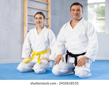 Smiling young woman and middle-aged man wearing kimono sitting in seiza position in sports hall - Powered by Shutterstock