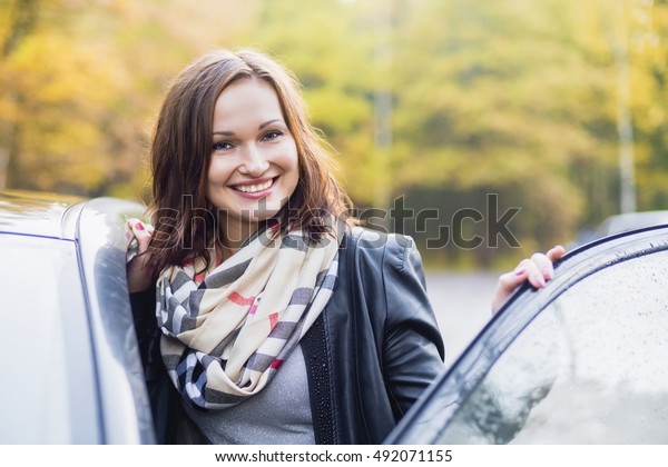 smiling young woman\
next to the open car\
door