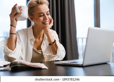 Smiling young woman on a video call via laptop computer while sitting at the table at home
