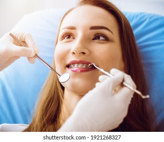 Lächelnde junge Frau mit kieferorthopädischen Klammern, die vom Zahnarzt in der sonnigen Zahnklinik untersucht wurde. Konzept für gesunde Zähne und Medizin