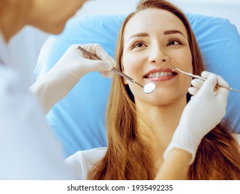 Lächelnde junge Frau mit orthodontischen Klammern, die vom Zahnarzt in einer Zahnklinik untersucht wurden. Konzept für gesunde Zähne und medizinische Versorgung