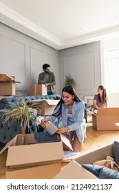 Smiling young woman packing her things in cardboard box as she moves into a new apartment while her roommates talk and help her in the background.. - Shutterstock ID 2124921137