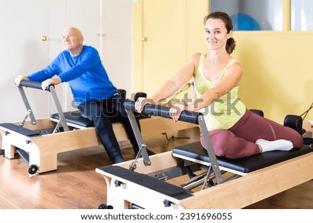 Smiling young woman performing set of pilates exercises on reformer in fitness studio..