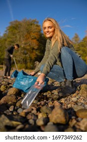 Smiling Young Woman Picking Up Plastic At Rocky Beach