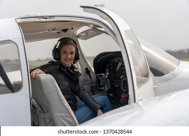 Smiling Young Woman Pilot With Headset Sitting in Cockpit of Private Aircraft. Portrait of attractive young woman with headset in cockpit. She is sitting in front of dashboard and looking at camera.