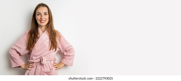 Smiling young woman in a pink bathrobe on a white background. Banner.