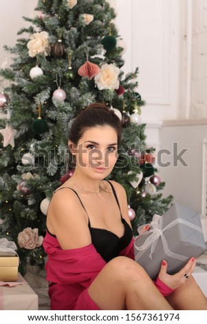 smiling young woman in a pink blouse with gingerbread and a cup of coffee sits by the New Year tree