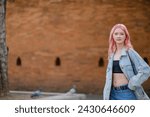 Smiling young woman with pink hair standing by wall. High quality.