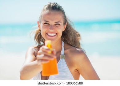 Smiling young woman pointing bottle of sun block creme in camera
