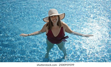 A smiling young woman in a pool wearing a wide-brimmed hat and burgundy swimsuit during summer. - Powered by Shutterstock